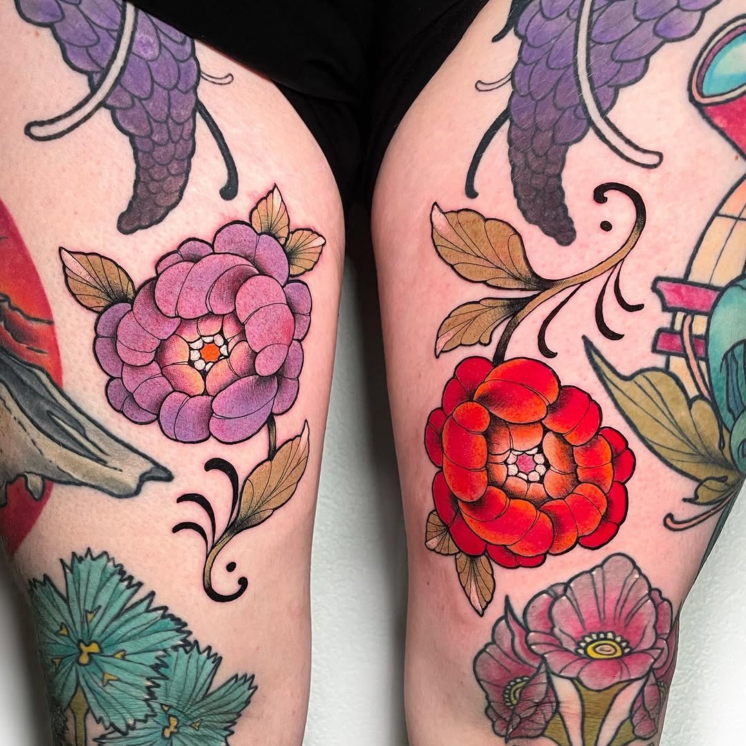 Two thighs display colorful botanical tattoos featuring purple and red clustered flowers with golden leaves, purple wings, and teal blooms against pink skin.
