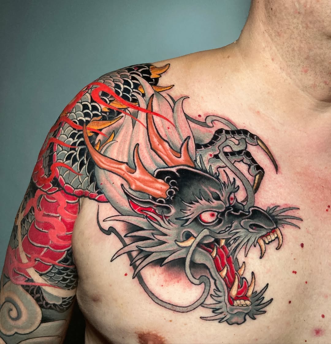 Dragon head and koi fish tattoo on shoulder and chest in red, black, orange, and gray with detailed scales and flowing design elements.