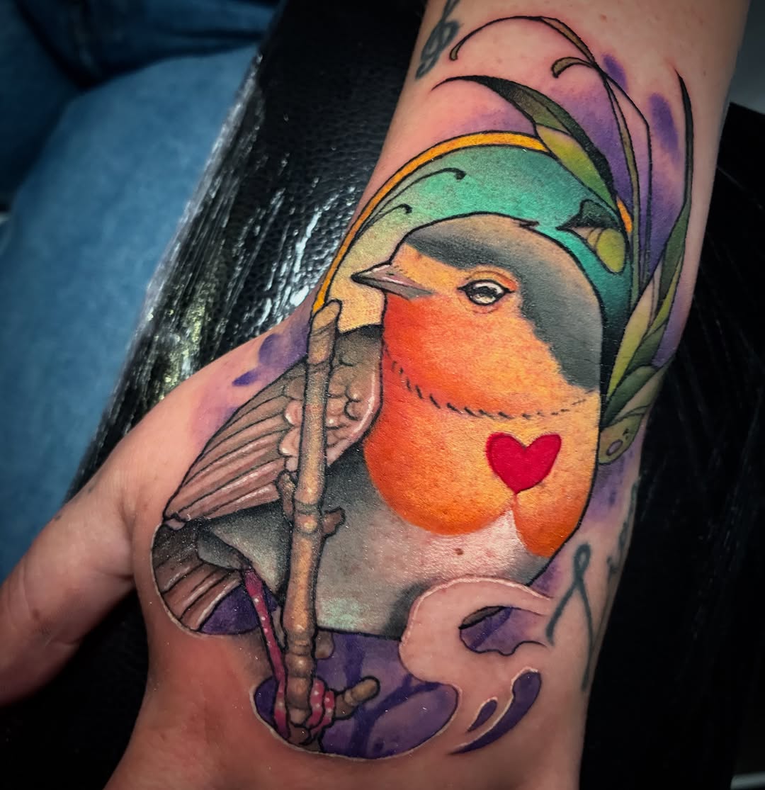 Colorful robin tattoo on arm featuring orange breast, green wings, red heart, purple background, and flowering branch detail.