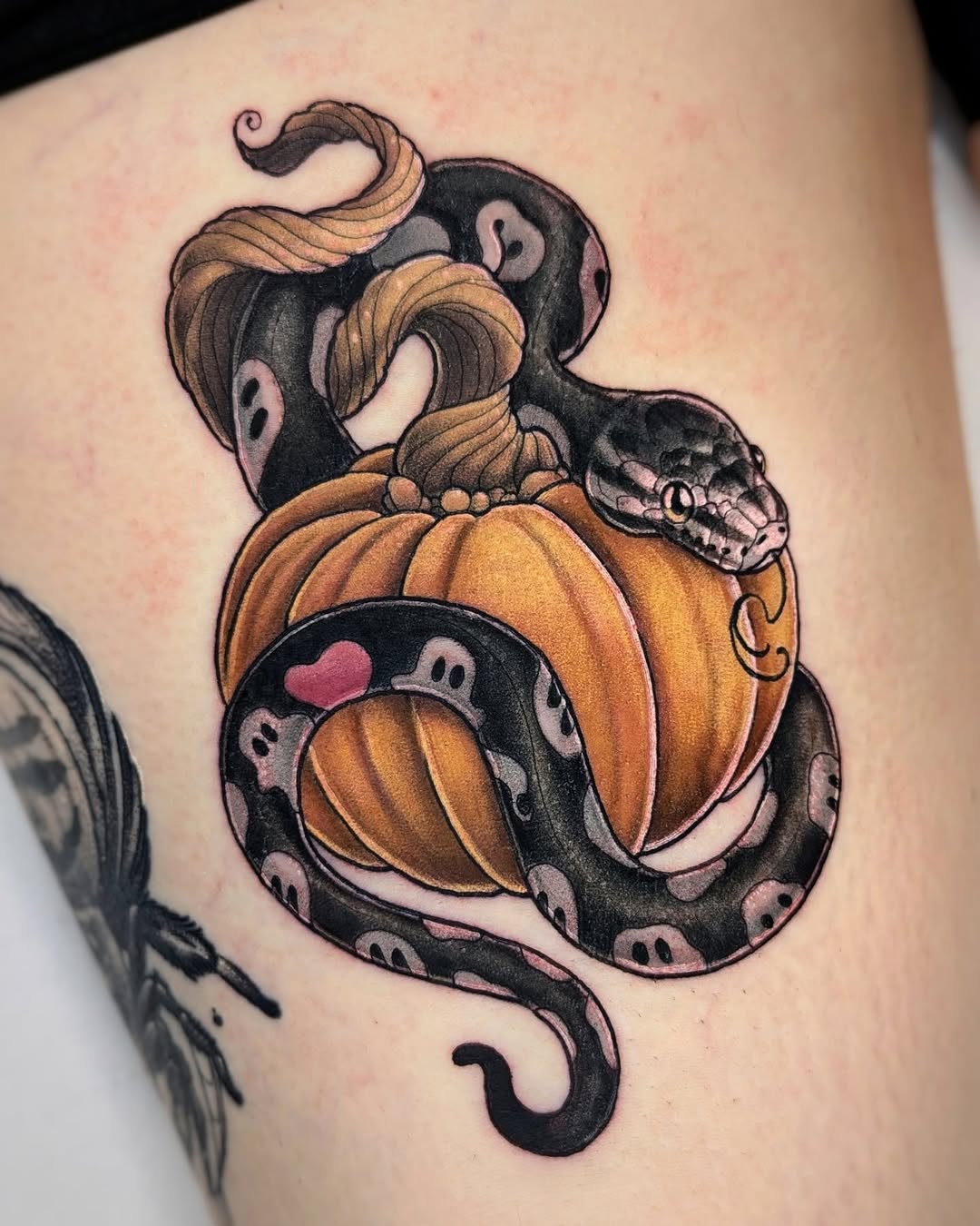 Colorful tattoo on upper arm featuring coiled snakes intertwined with orange pumpkins and small skull details, with pink accents throughout.