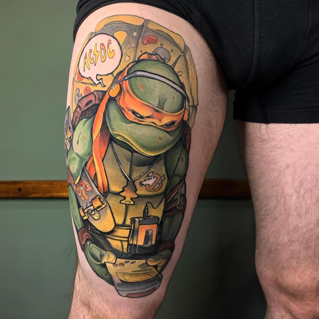 Colorful thigh tattoo featuring a green turtle character wearing an orange mask and holding pizza, with "ACDC" speech bubble and additional cartoon elements in yellow and red tones.