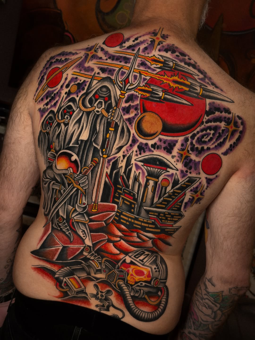 Large colorful back tattoo featuring a mechanical skull with red and gold accents, surrounded by purple cosmic patterns, planets, and architectural elements.
