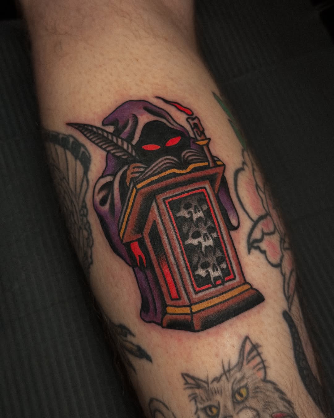 Colorful tattoo on an arm depicting a demonic purple face with red eyes and an ornate red and gold chest piece containing skull designs.