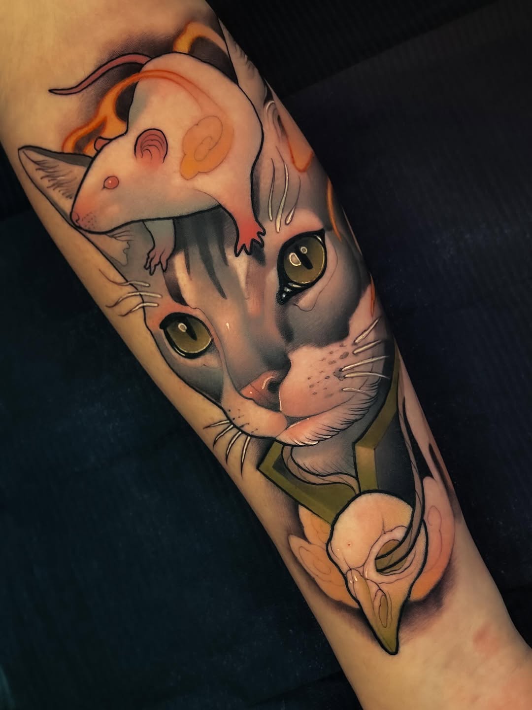 Two stacked cat faces with golden eyes and orange/peach coloring on the forearm, featuring detailed whiskers and shading in black, orange, and cream tones.