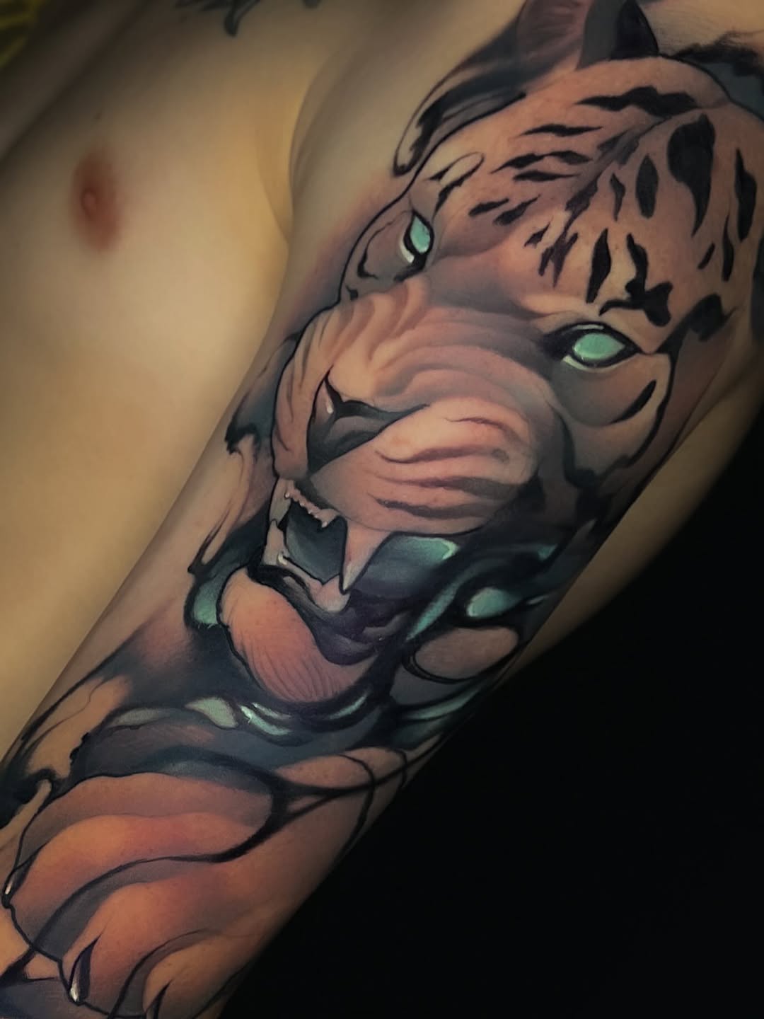 Tiger head tattoo on forearm with glowing green eyes, brown and black coloring, showing detailed facial features and striped markings.