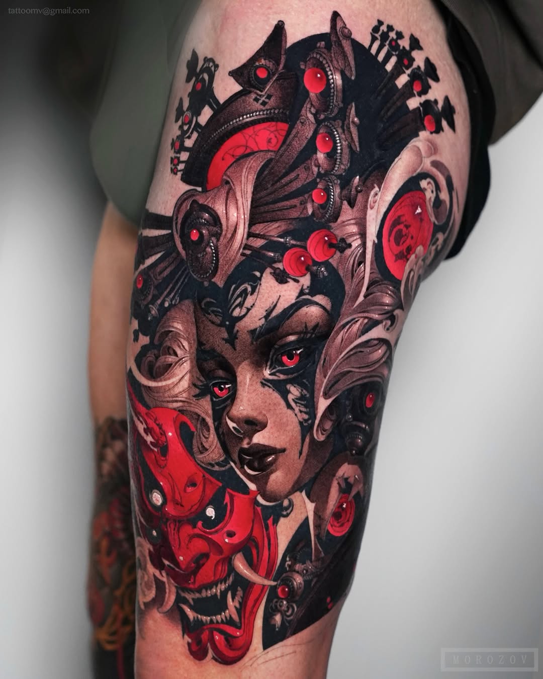 Colorful tattoo on upper thigh featuring a woman's face with red glowing eyes, mechanical creatures, ornamental designs, and Japanese characters in black, red, and skin tones.