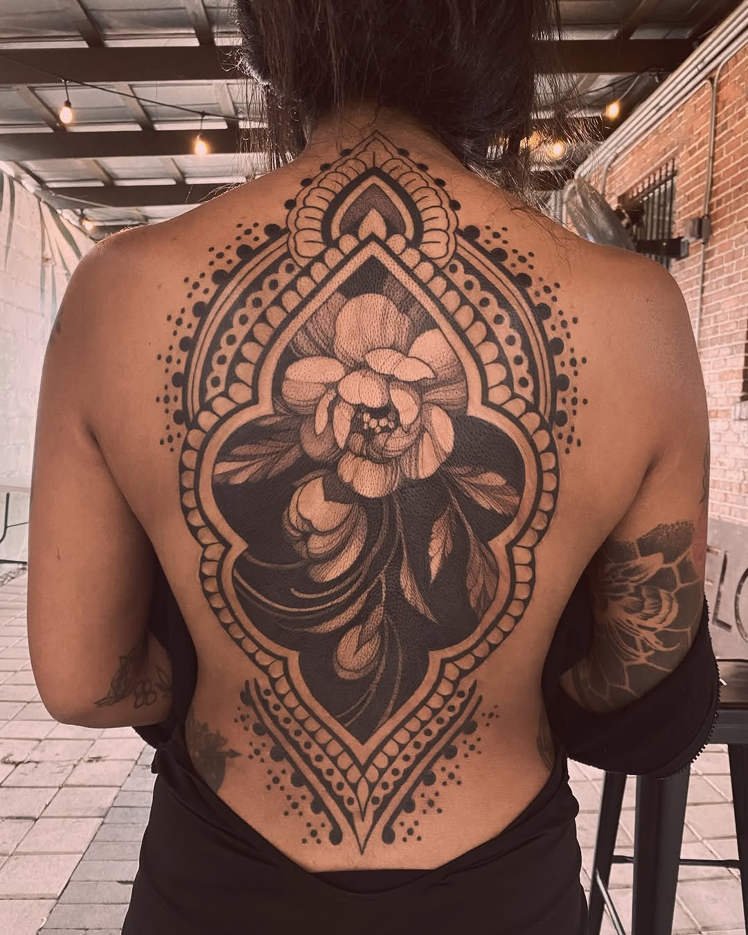Large back tattoo featuring a ornamental teardrop frame with a detailed peony flower in the center, done in black ink with shading.