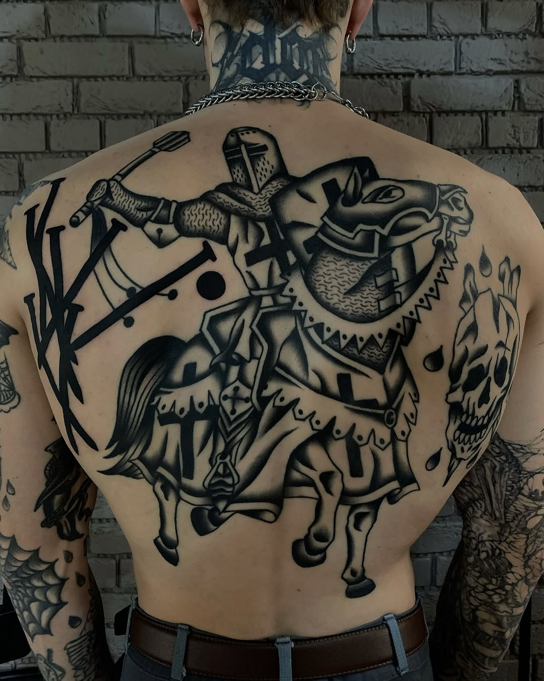 Medieval knight on horseback with sword and shield tattooed across back in black ink with detailed armor and decorative elements.