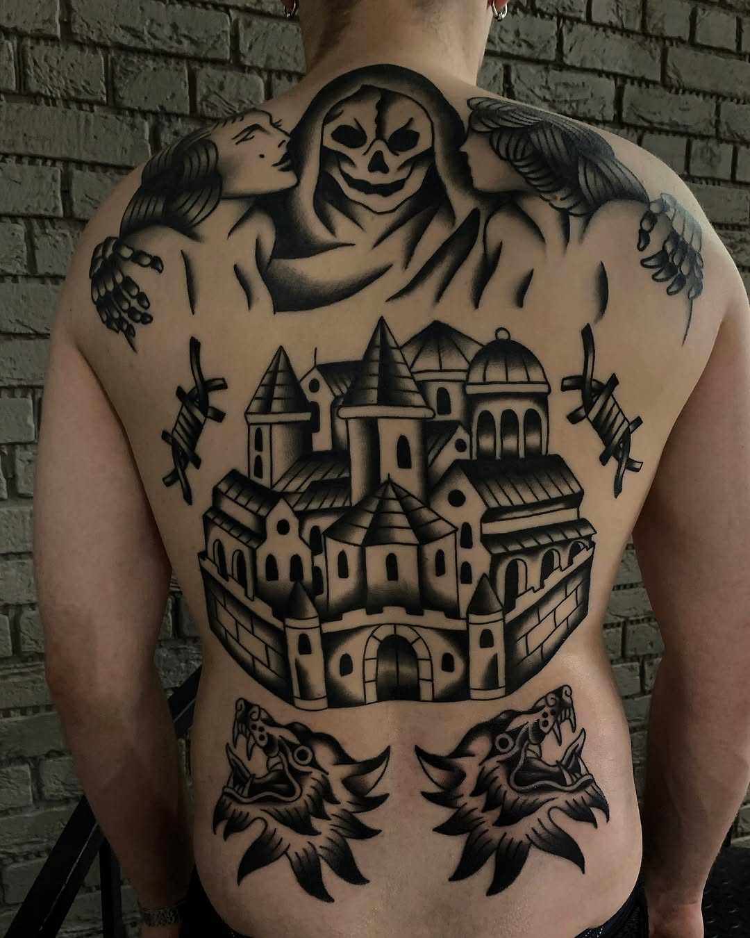 Back tattoo featuring a skull-faced grim reaper with winged figures, a multi-towered castle, two wolves, and decorative elements in black ink.