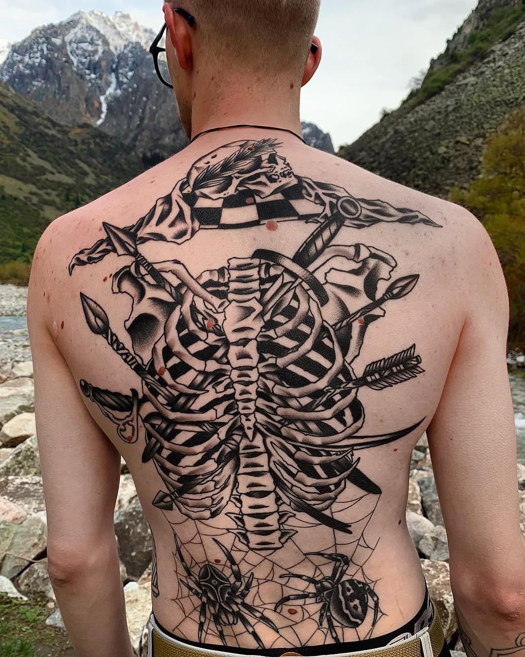 Large-scale skeletal ribcage with skull, anatomical spine, and decorative elements including spiderwebs and flora, covering the entire back in black ink.