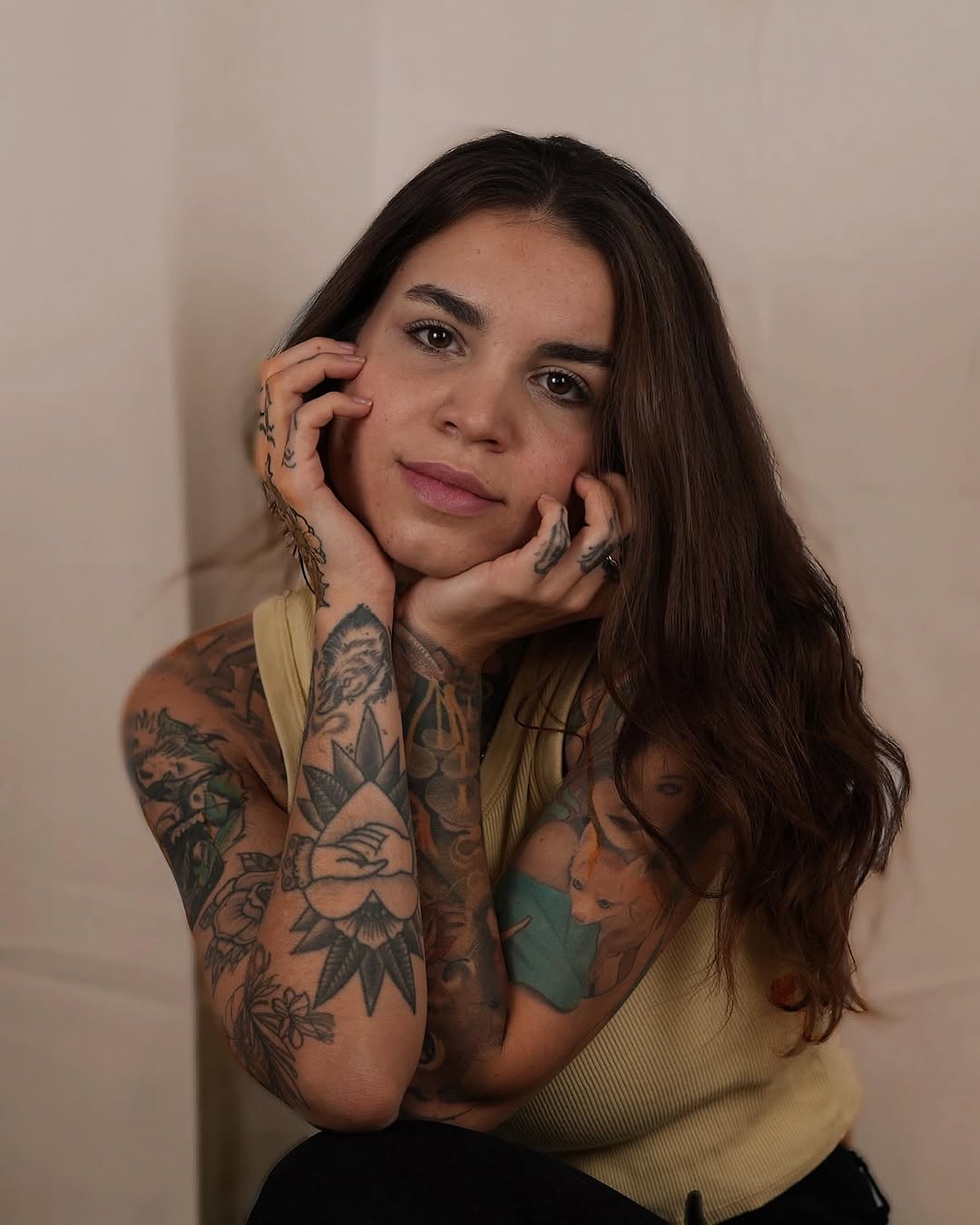 Portrait of a woman with extensive floral and botanical tattoos covering both arms in black and gray ink on her shoulders and upper body.