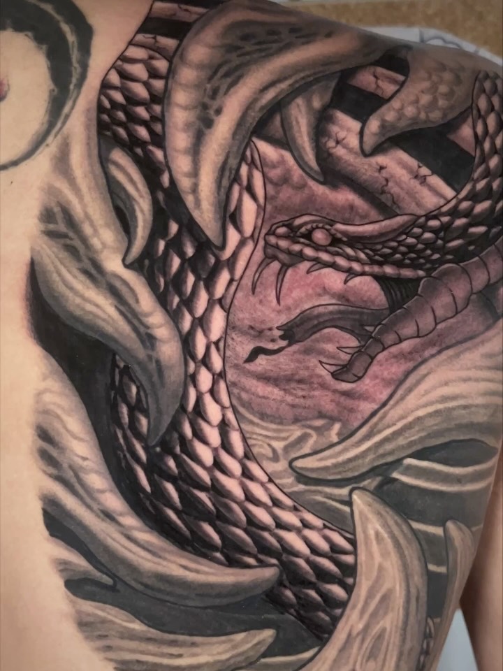 Dragon head tattoo with scaled texture and flowing mane details in black and gray ink on the upper chest and shoulder.