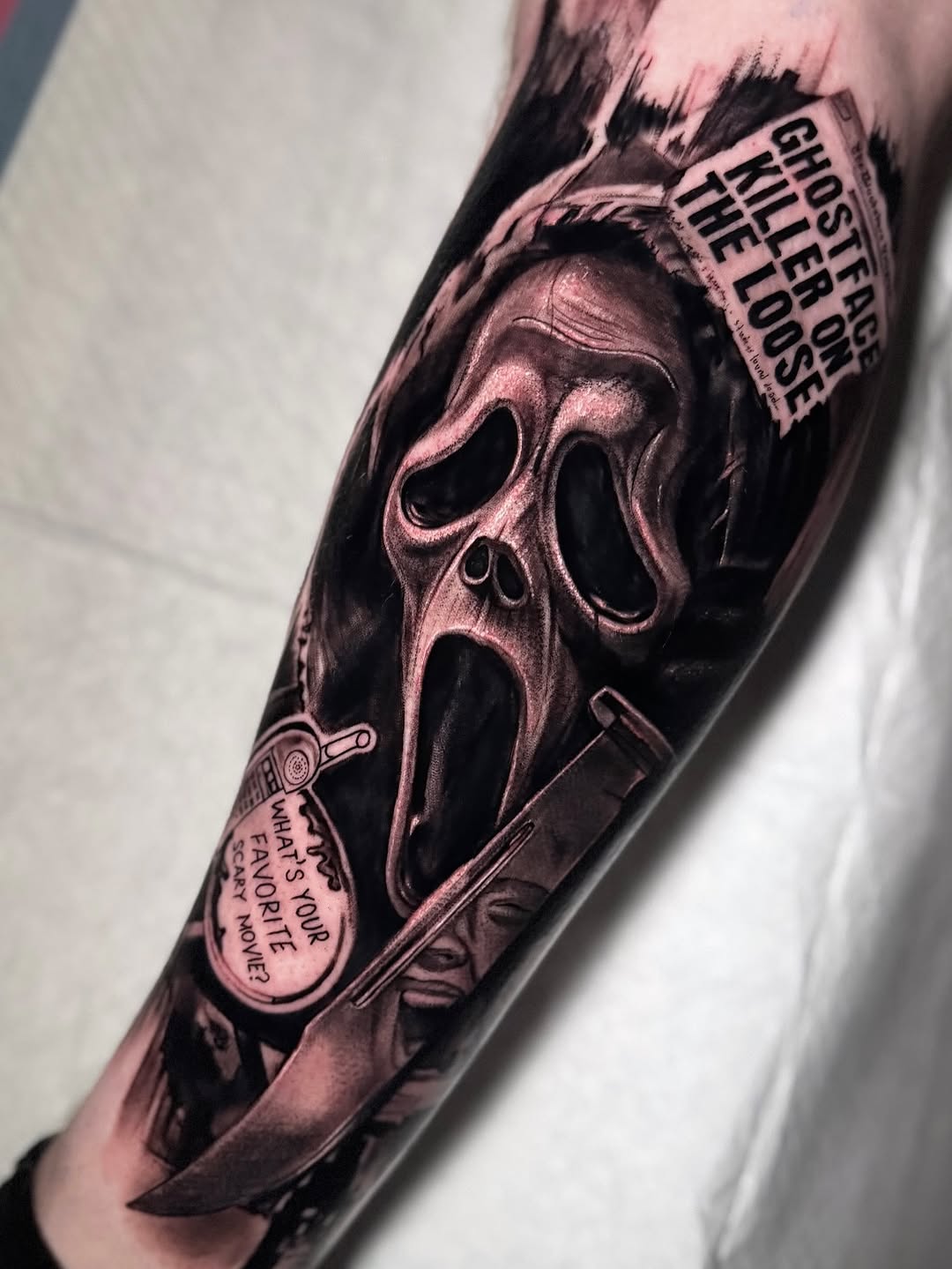 Screaming ghost mask tattoo on forearm with knife, film reel, and text quotes in shades of gray and brown ink.