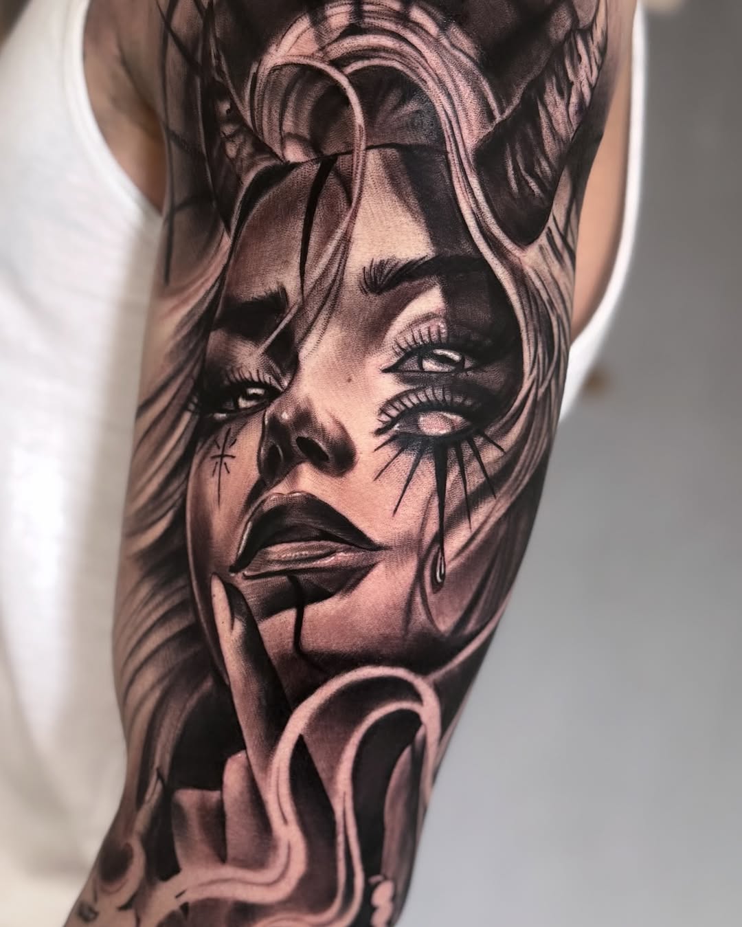 Portrait tattoo of a woman's face with dramatic eye makeup and flowing hair, featuring ornamental curved lines, on the upper leg in grayscale tones.