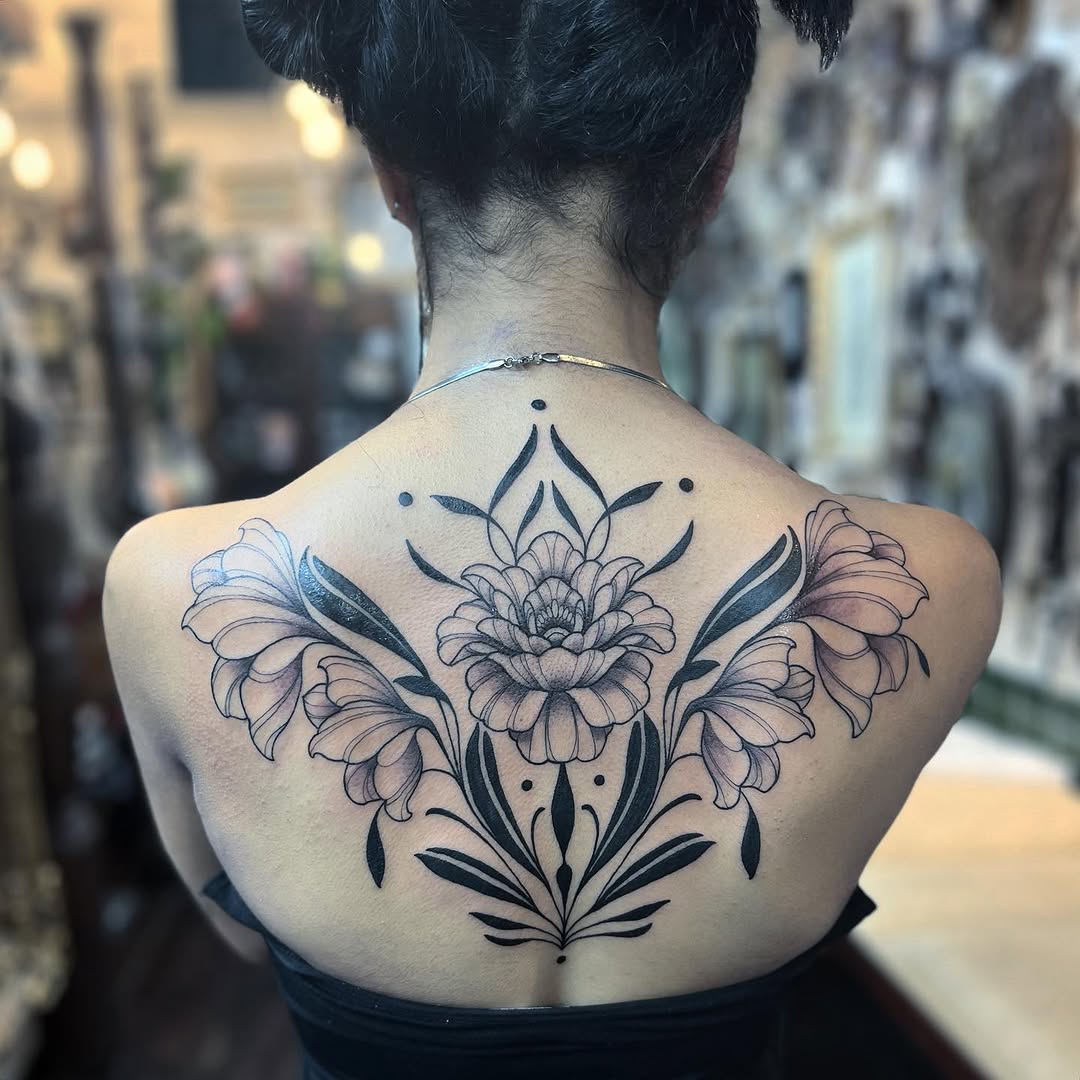 Back tattoo featuring symmetrical lotus flowers with decorative leaves and geometric elements in black and purple ink on pale skin.