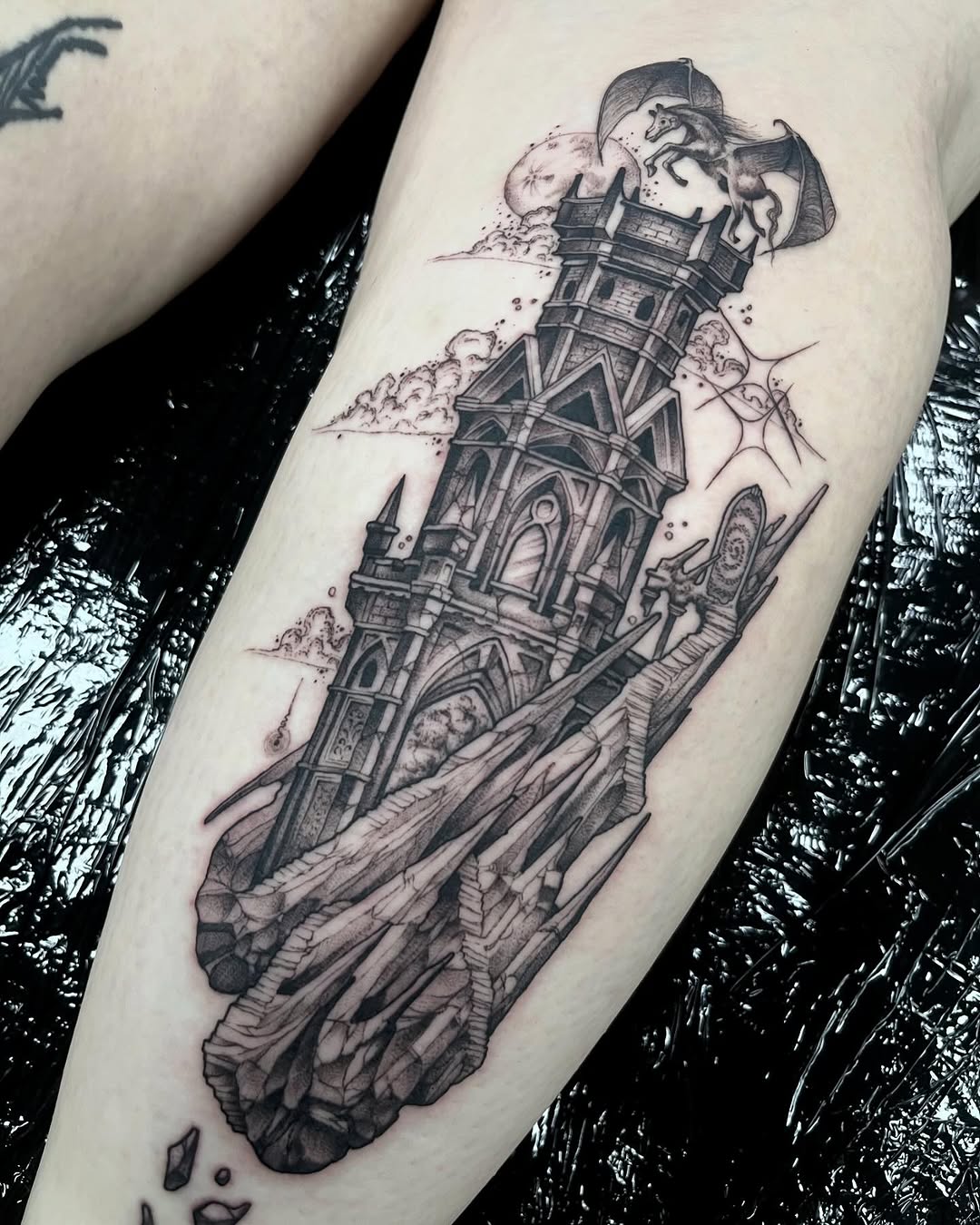 Tall architectural tower with multiple levels and ornate windows topped by mythological creatures, rendered in black ink on the inner forearm.