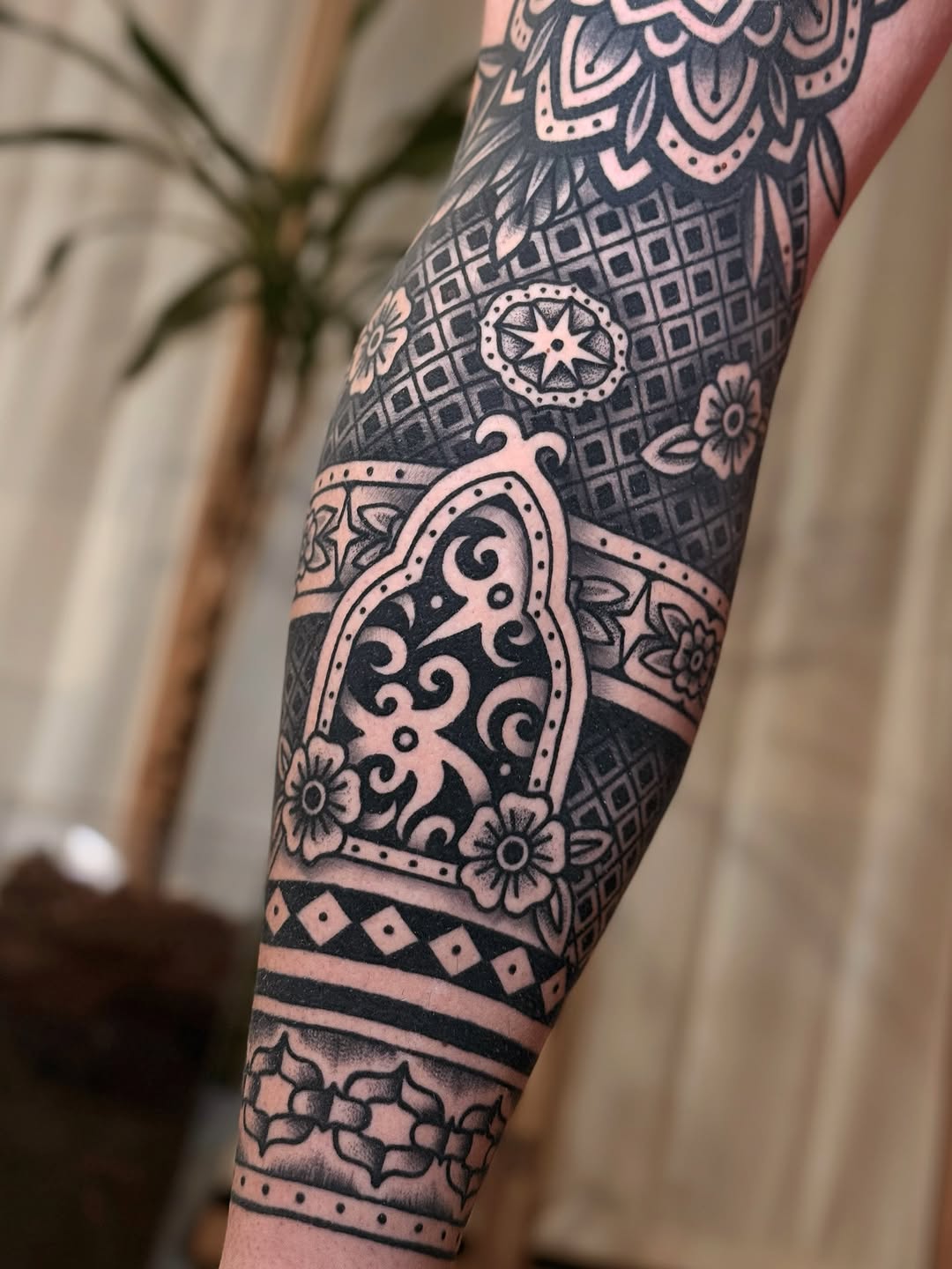 Detailed ornamental forearm tattoo featuring geometric patterns, floral motifs, and decorative borders in black and pink ink.