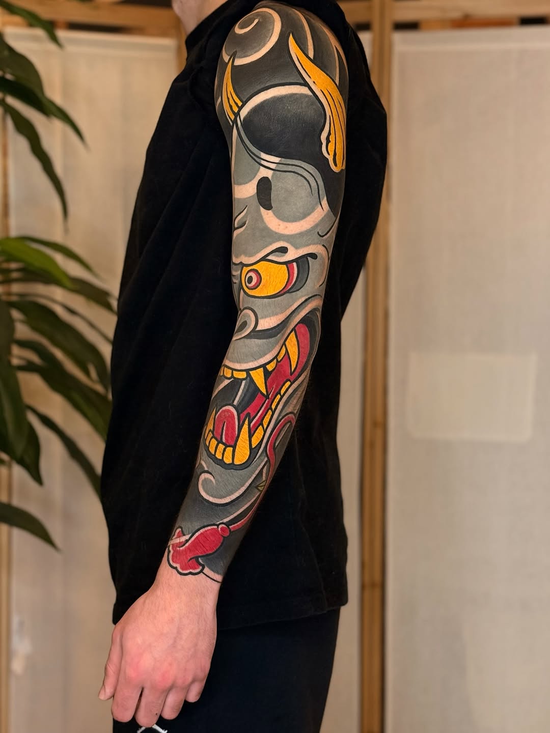 Full-sleeve arm tattoo featuring a skull with horns, fish, and decorative elements in gray, gold, red, and cream colors.