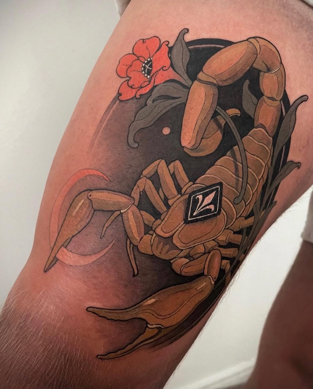 Colorful tattoo on an upper arm featuring a brown crab holding a red flower, with green foliage and a small diamond symbol on its claw.