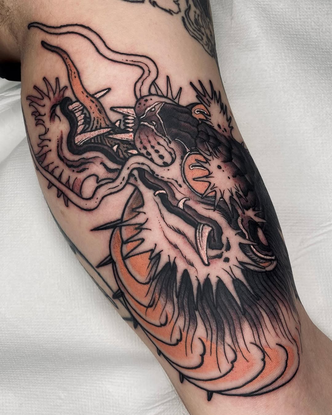Colorful demon or oni head tattoo on an arm featuring orange and black ink with spiky features and ornate details.