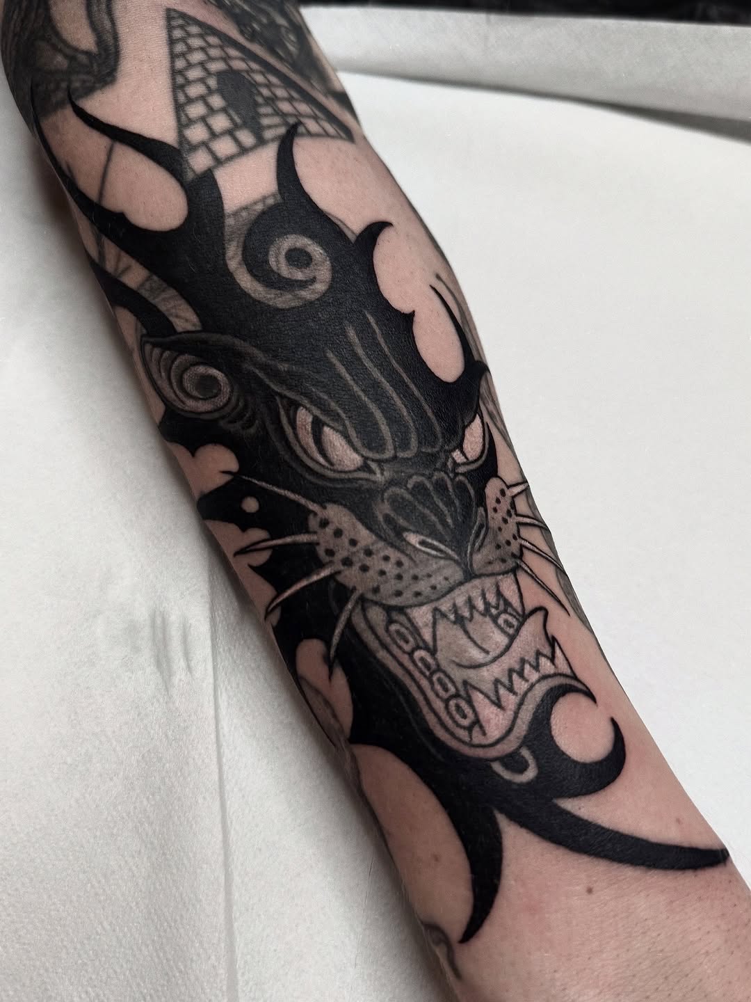 Monochromatic bat and skull sleeve tattoo with geometric patterns and shading on the forearm and upper arm.
