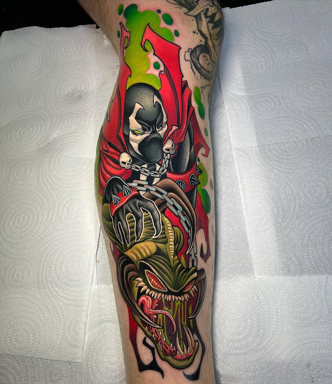 Colorful leg tattoo featuring a skeletal figure in a red cloak above a monstrous green creature with bared teeth, displayed on the calf.