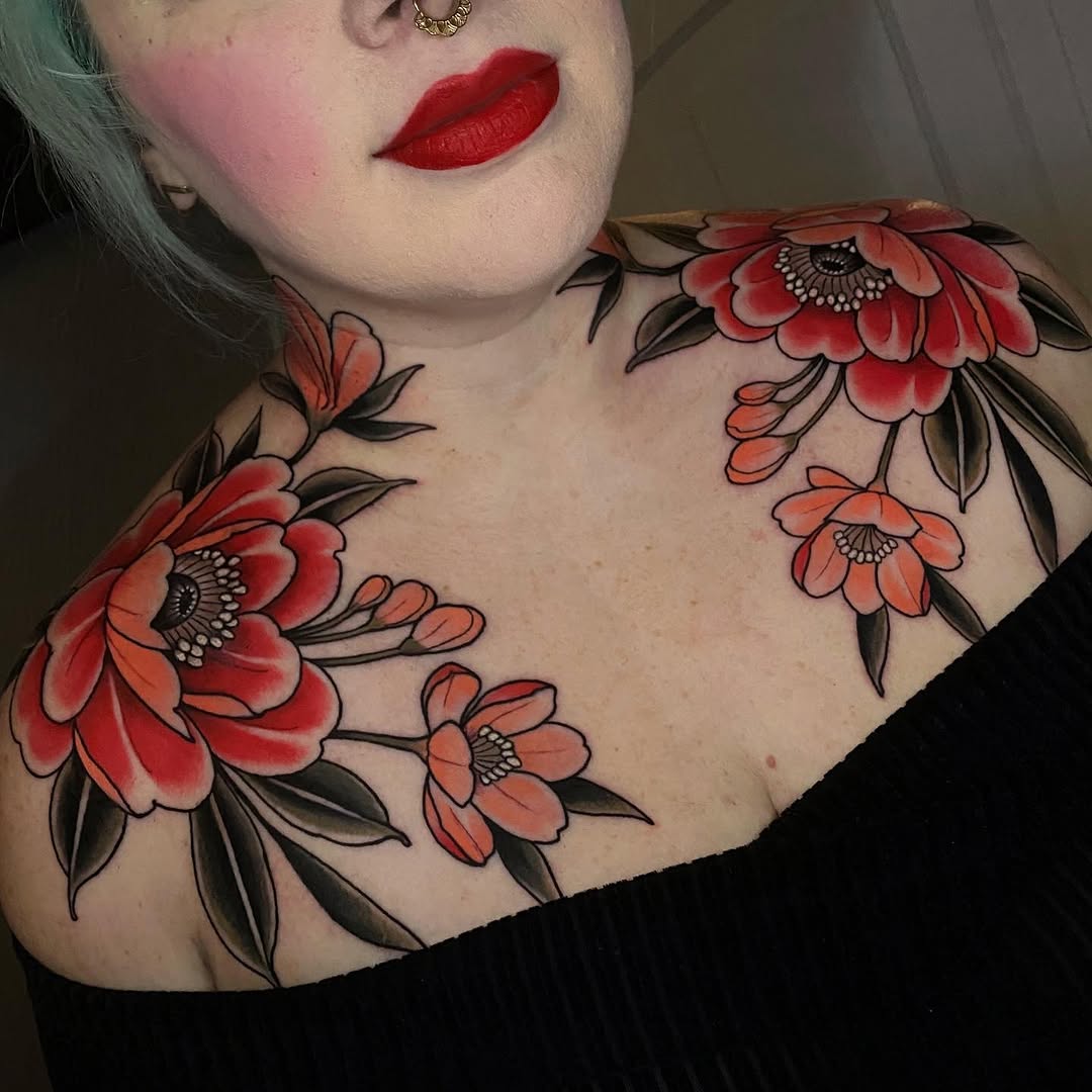 Colorful floral shoulder and chest tattoos featuring red and orange peonies with black leaves and detailed centers on pale skin.