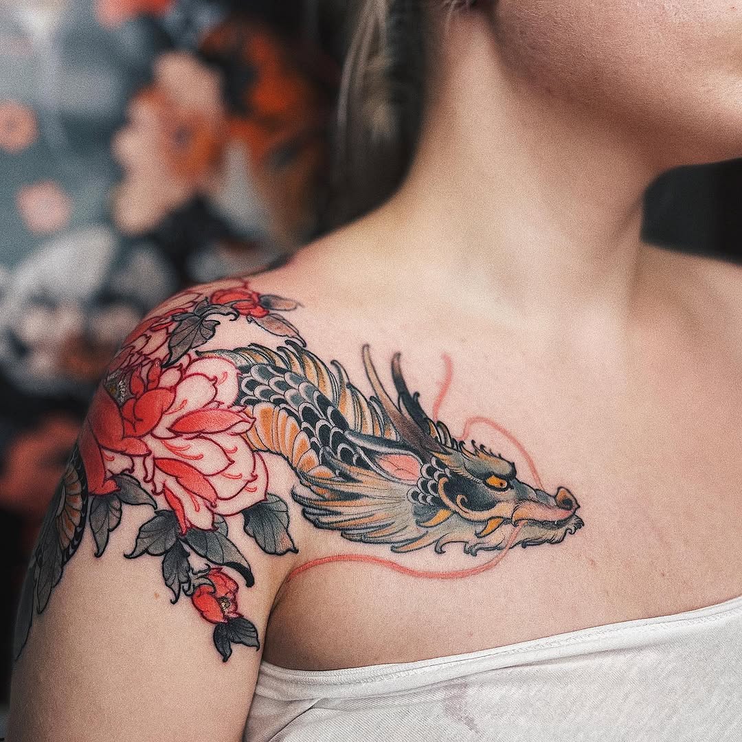 Colorful shoulder tattoo featuring a dragon head with red and orange peonies, black linework, and a red curved tail element on pale skin.