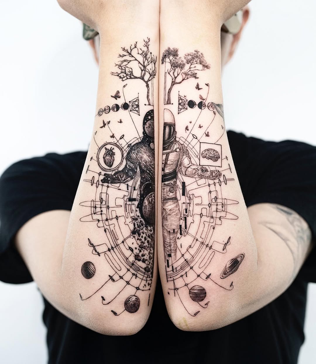 Matching forearm tattoos featuring bare trees, astronauts, celestial bodies, anatomical organs, and flying birds in black ink on pale skin.
