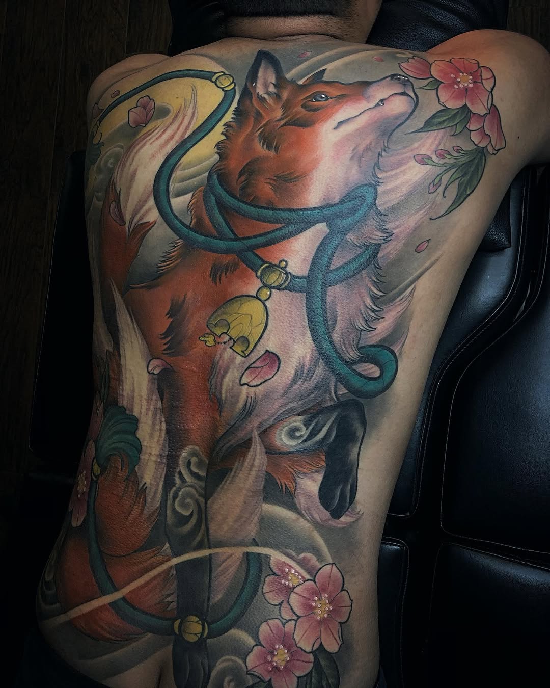 Large back tattoo featuring a brown fox head with teal serpents, yellow moons, and pink flowers on the shoulder and thigh area.