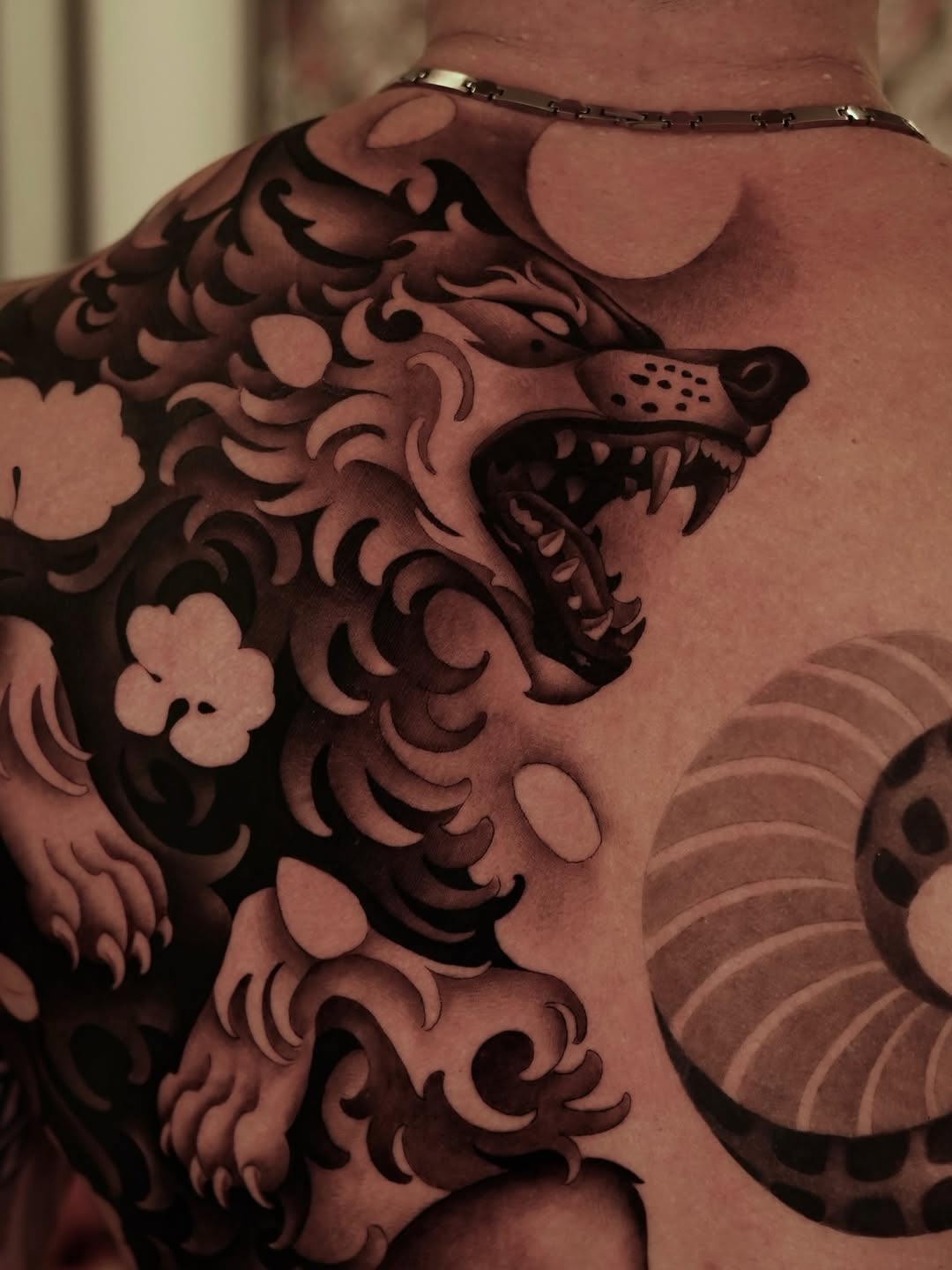 Large fierce dragon tattoo covering the shoulder and chest in black ink with ornate scrollwork and floral details on tan skin.