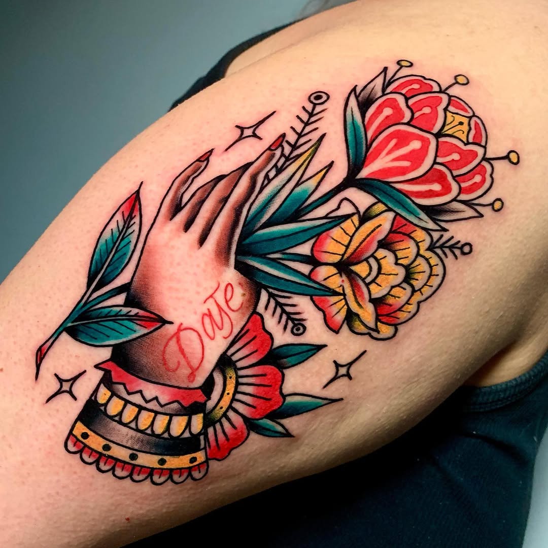 Hand with colorful flowers in red, yellow, and teal, featuring decorative bands and small stars, tattooed on the upper arm.