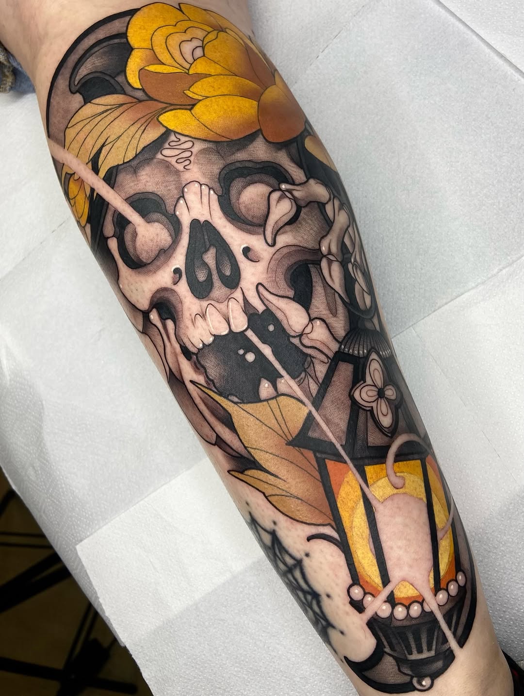 Skull tattoo with golden flowers and geometric lower leg design in color and black ink on the calf.