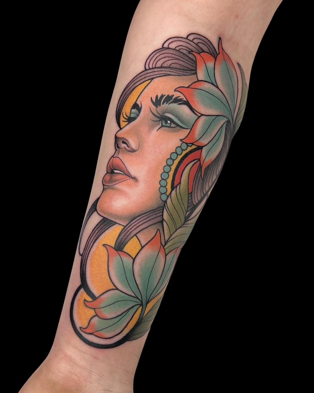 Colorful portrait tattoo on forearm featuring a woman's profile with flowers, pearl earring, and flowing hair in orange, green, and red tones.