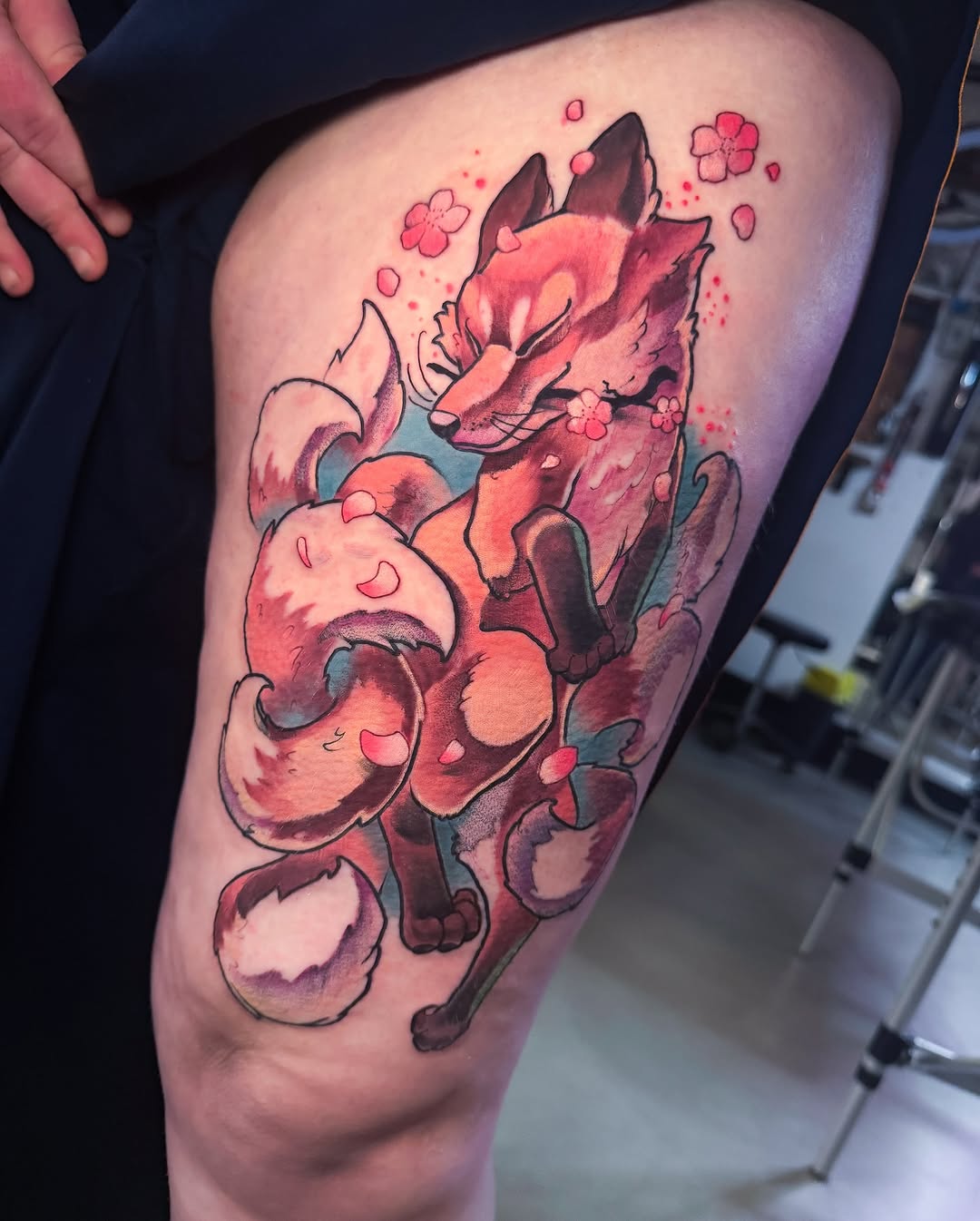 Colorful thigh tattoo featuring a fox with flowing tail surrounded by pink flowers and petals in red, orange, and teal tones.