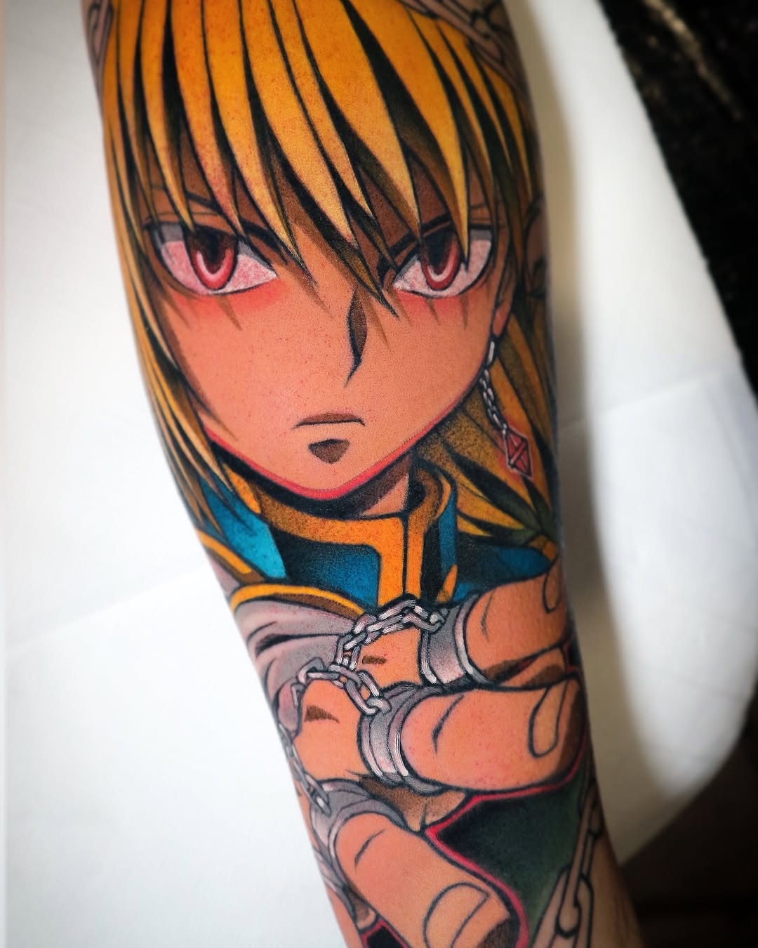 Colorful tattoo on forearm featuring an anime-inspired character with orange hair and pink eyes, wearing blue and orange clothing with arm bands.