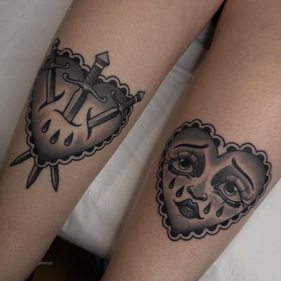 Two black ink tattoos on forearms: a sacred heart with swords and clouds on one arm, and a face with tears and closed eyes on the other.