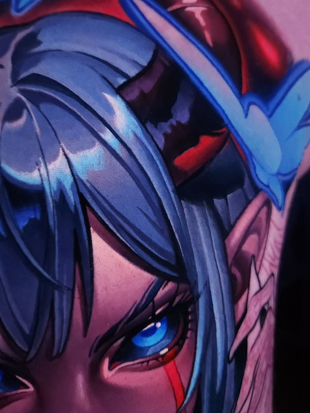 Close-up portrait tattoo featuring a character with long blue hair and bright blue eye, rendered in vibrant blue, red, and pink tones.