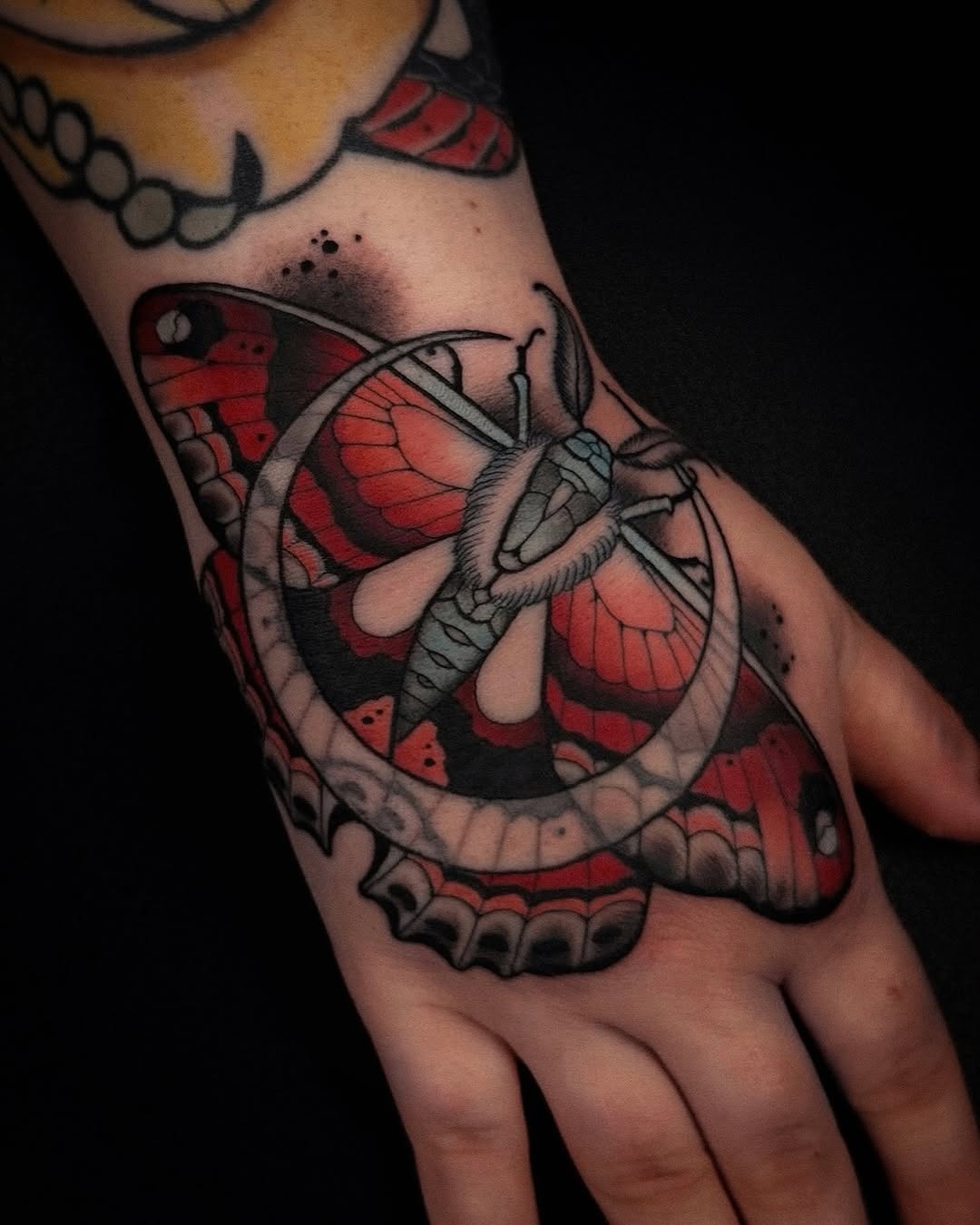 Detailed butterfly tattoo on hand featuring red and black wings with intricate line work and shading on the palm and fingers.