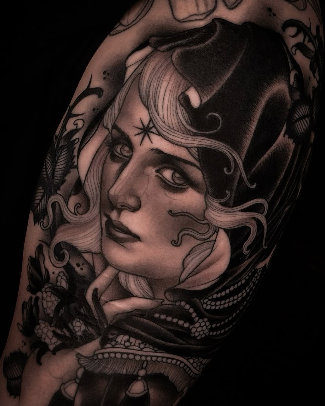 Detailed portrait tattoo of a woman's face with flowing wavy hair, decorative elements, and ornamental details on the arm, rendered in black and grey ink.