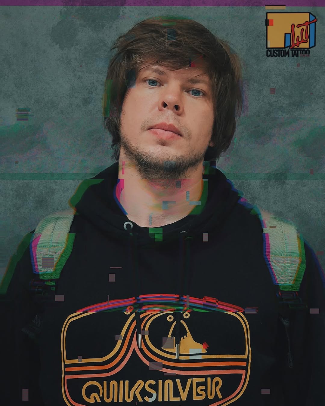 Man wearing black hoodie with large colorful chest tattoo featuring stylized eyes, orange and gold curved lines, and "QUIKSILVER" text in gold lettering.