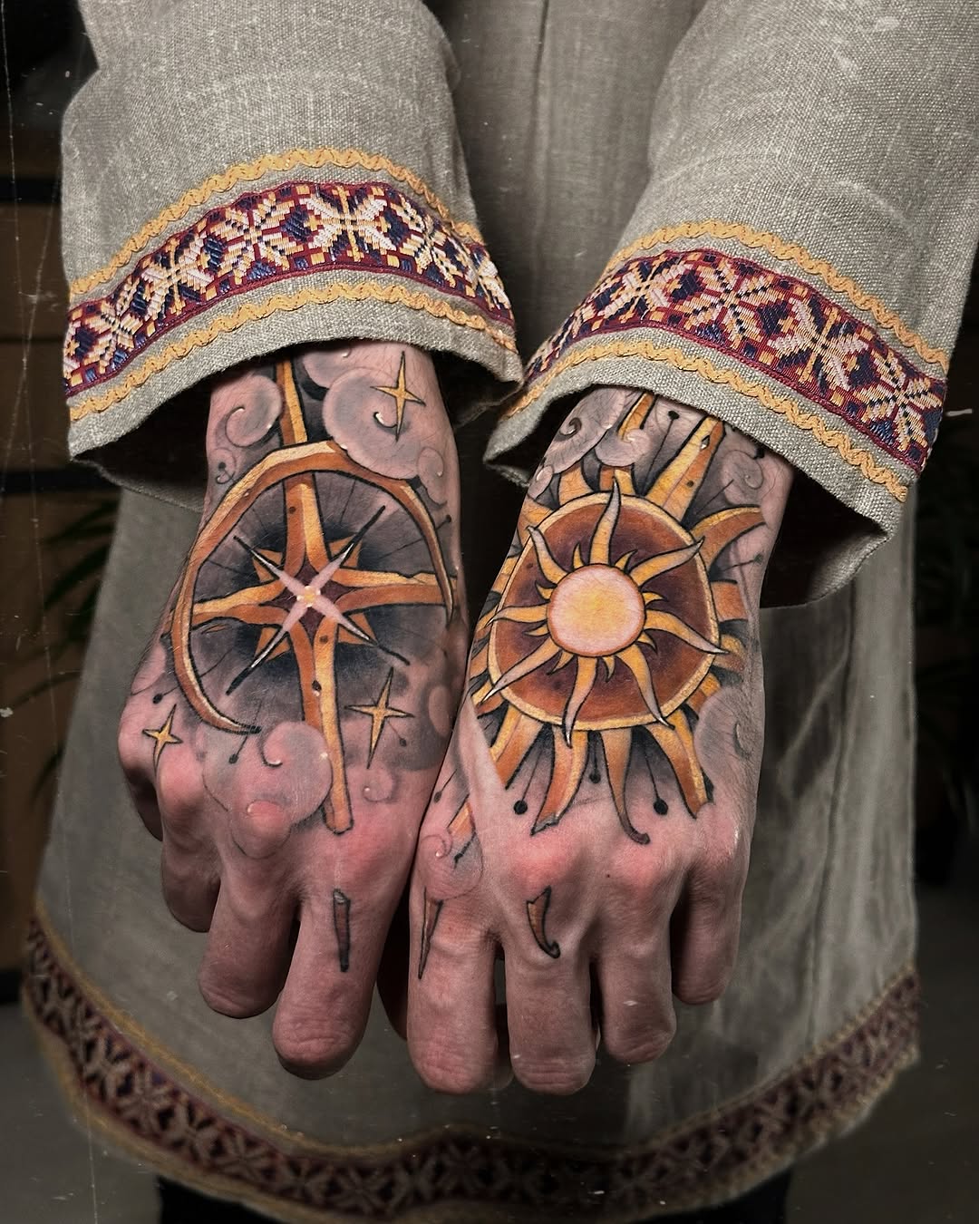 Hands display matching sun and crescent moon tattoos in gold and burgundy on the backs, paired with decorative cuffed sleeves.