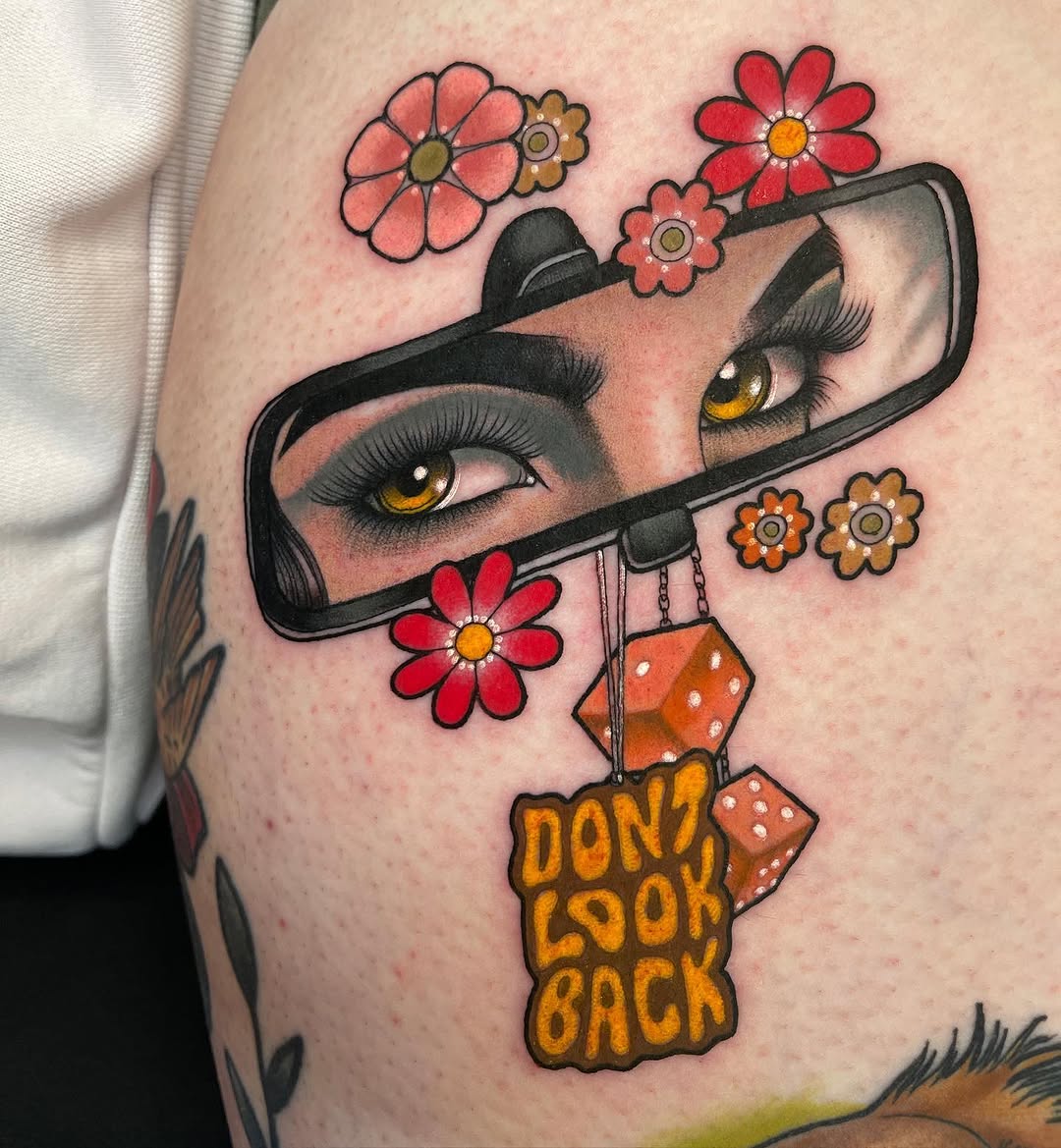 Colorful tattoo on upper arm featuring a woman's face in a phone mirror with flowers and dice, text reading "Don't Look Back" below.
