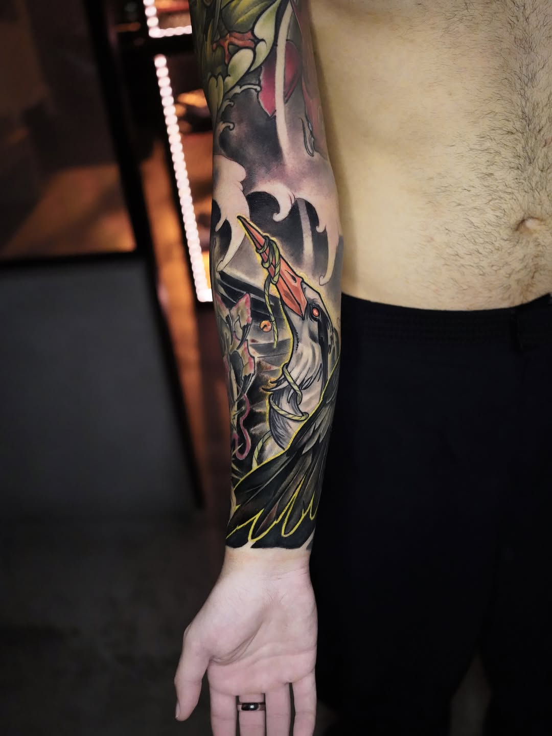 Colorful full-sleeve arm tattoo featuring mythological creatures and ornamental designs in red, yellow, black, and purple tones.