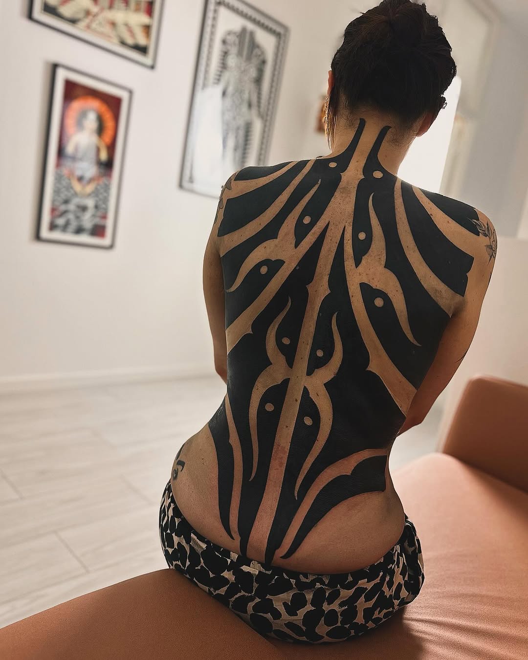 Back tattoo featuring organic curved lines in black and tan creating a symmetrical pattern from shoulders to lower back, displayed in a studio setting.