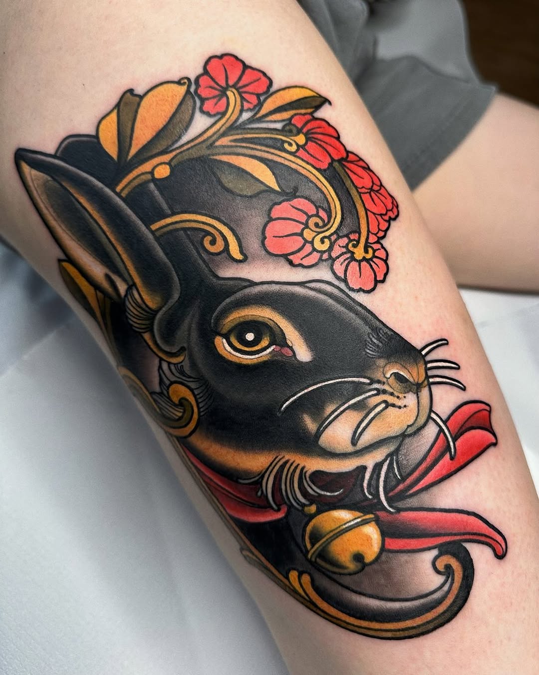 Black rabbit head with golden accents, pink and red flowers blooming from its crown, ornamental scrollwork, and red ribbon detail on the upper arm.