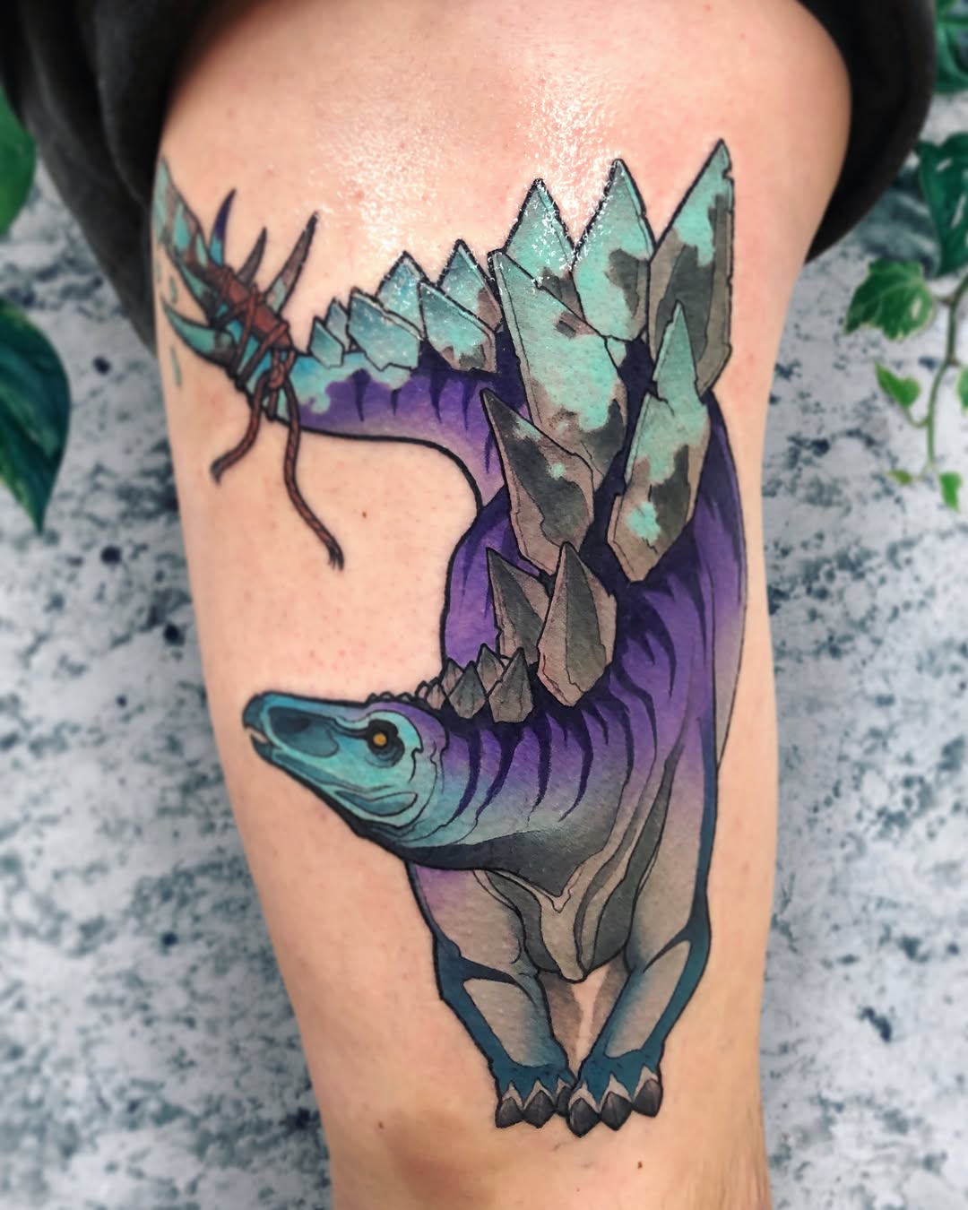 Colorful tattoo on thigh featuring a turtle with turquoise head, purple body, gray-green crystalline shell, and spiky antennae, surrounded by purple shading.