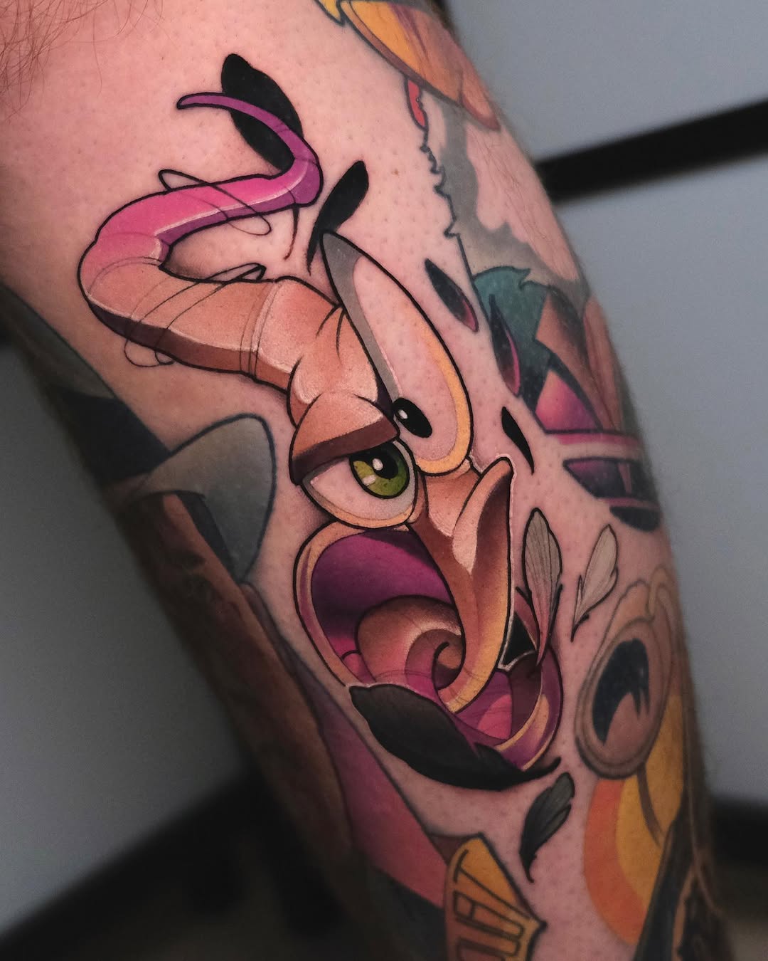 Colorful leg tattoo featuring an expressive character with pink tentacles, yellow eyes, and an open mouth in shades of orange, pink, and yellow.