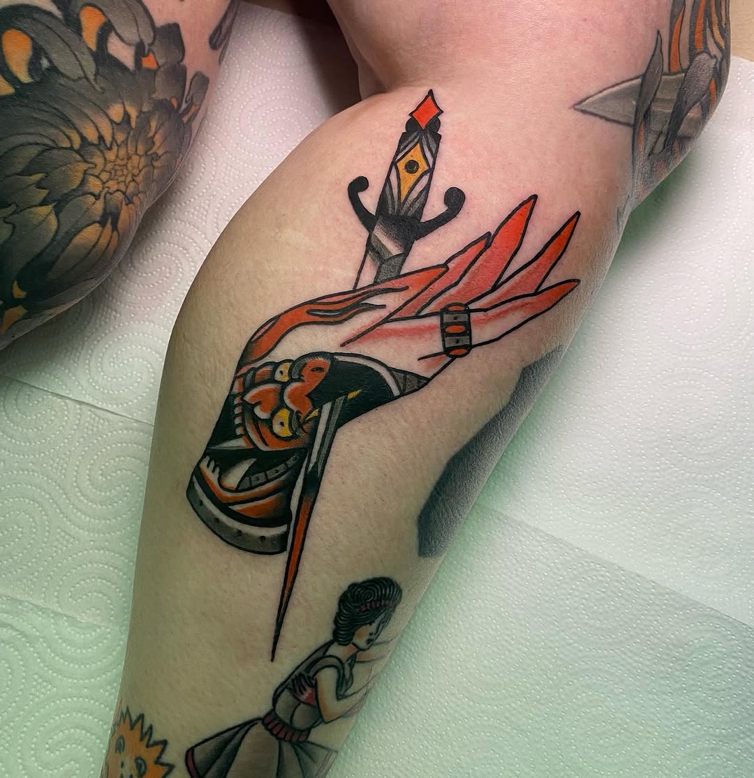 Colorful tattoo on an arm featuring a hand holding a dagger with red flames and a candle with an eye, surrounded by decorative elements.