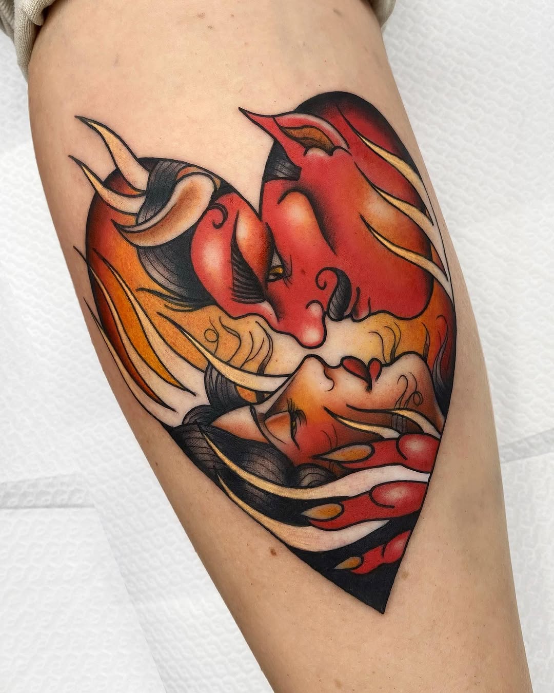 Colorful tattoo on upper arm featuring two stylized demon or oni faces in red, orange, and black with flowing hair and curved horns.